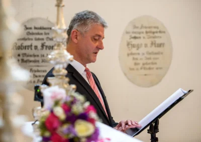 Mann liest bei Trauung in Schloss Aufhausen vor, umgeben von Blumenarrangement und Dekoration.
