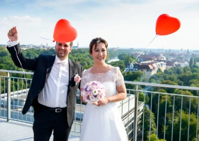 Brautpaar mit Herzballons auf Hochzeitsfeier in München. Blick vom Hilton im Tucherpark auf die Skyline.