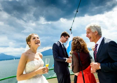 Brautpaar lacht mit Gaesten bei einer Hochzeit im Hotel Aiterbach am Chiemsee. Stimmungsvoll und glanzvoll.