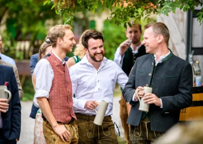 Hochzeit in Geitau: Feiernde Gaeste in traditioneller Tracht beim Hasenoehrlhof nahe Bayrischzell, lachend im Freien.