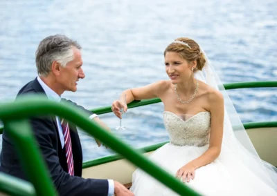 Braut auf dem Boot bei Hochzeit im Hotel Aiterbach, Chiemsee, in einem eleganten Hochzeitskleid mit Hintergrundsee.
