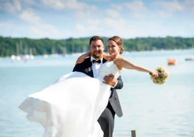 Brautpaar vor dem Ammersee bei sonniger Hochzeit im Seehaus Schreyegg in Stegen. Feierliche Momente am Wasser.