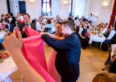 Brautpaar schneidet Herz aus Stoff während Hochzeit in Schloss Seefeld, festlich geschmückter Saal voll Gästen.