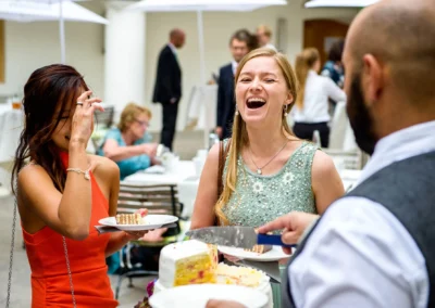 Gäste lachen bei Hochzeit im Schloss Hohenkammer. Hochzeitsreportage zeigt fröhliche Momente beim Kuchenessen.