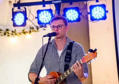 Musiker mit Gitarre und Mikrofon bei Hochzeitsfeier, Schloss Pertenstein, Traunreut, stimmungsvolle Beleuchtung.