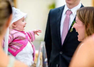 Lachendes Baby mit pinker Strickjacke lacht mit Frau, Hochzeit Schloss Hohenkammer, festgehalten vom Hochzeitsfotografen.