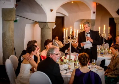 Hochzeitsfeier im Schloss Amerang, Gaeste bei Kerzenschein lauschen Rede, festliche Trauung im Chiemgau.