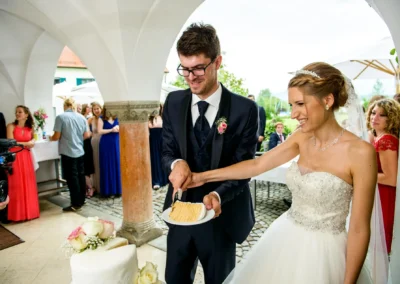 Brautpaar schneidet Hochzeitstorte im Hotel Aiterbach am Chiemsee, lachende Gesichter und festliche Stimmung.