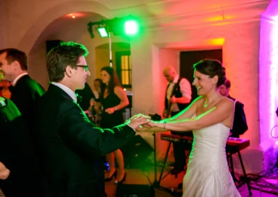 Brautpaar tanzt bei Hochzeit im Schloss Amerang, begleitet von Band und farbenfroher Beleuchtung, Hochzeitsfeier-Reportage.