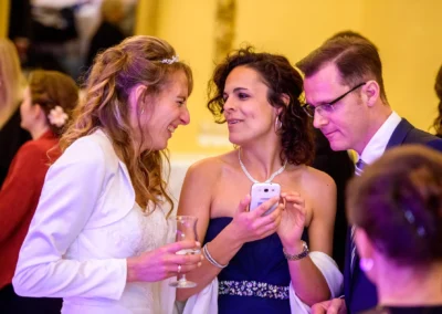 Hochzeitsszene im Schloss Aufhausen: Gruppe von Gaesten lacht und betrachtet ein Smartphone waehrend der Hochzeitsfeier.