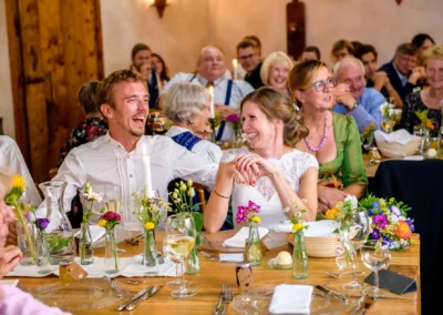 Hochzeitsfeier im Hasenoehrlhof, Gaeste lachen am Tisch, Geitau, Bayern.