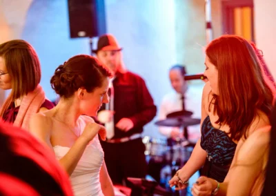 Hochzeitsreportage Schloss Amerang: Gaeste tanzen freudig bei einer Hochzeit mit Live-Band im Hintergrund.