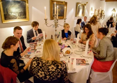 Gäste sitzen bei einer Hochzeitsfeier im Schloss Aufhausen am gedeckten Tisch mit Kerzenleuchter und Zeitung in der Hand.