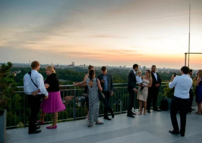 Hochzeitsfeier in München bei Sonnenuntergang auf einer Terrasse, Gäste und Fotograf mit Blick auf die Skyline.
