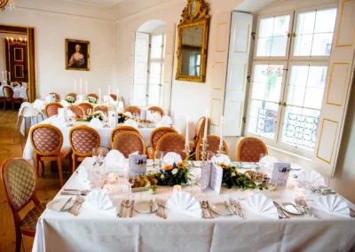 Elegante Hochzeitsfeier im Schloss Pertenstein, gedeckte Tische mit Kerzenleuchtern und Blumengestecken.