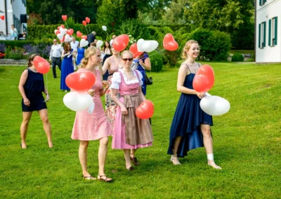 Hochzeitsgaeste mit Herzballons im Garten vom Hotel Aiterbach am Chiemsee, frische Sommerstimmung.