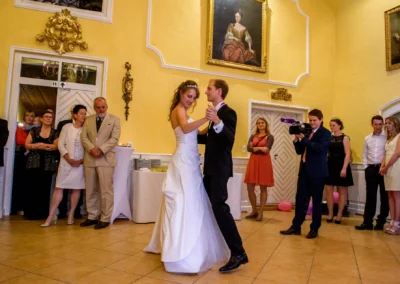 Brautpaar tanzt bei Hochzeit in Aufhausen, elegant gekleidete Gaeste beobachten, gelber Raum mit dekorativer Kunst.
