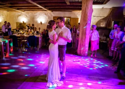 Brautpaar tanzt auf Hochzeit im Hasenoehrlhof Geitau, festlich erleuchteter Raum, Gaeste schauen zu.