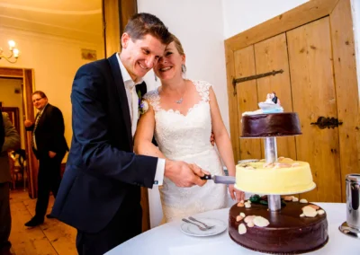 Brautpaar schneidet dreistoeckige Hochzeitstorte bei Feier auf Schloss Pertenstein, Traunreut. Hochzeitsglueck.