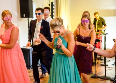 Gaste tanzen bei einer Hochzeit auf Schloss Hohenkammer, Freude beim Feiern. Hochzeitsreportage mit bunten Kleidern.