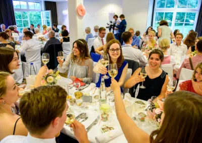 Hochzeitsfeier im Hotel Aiterbach am Chiemsee, Gaeste stossen mit Weinglaesern an und geniessen die Stimmung.