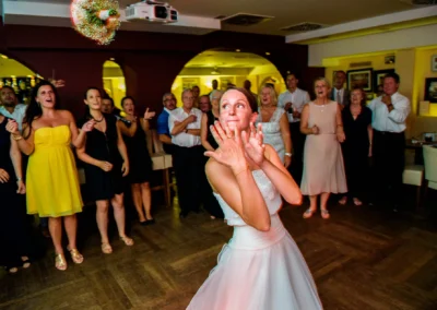 Braut wirft Blumenstrauss bei abendlicher Hochzeitsfeier in Muenchen, Gaeste beobachten gespannt.