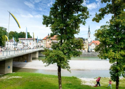 Blick auf die Stadtpfarrkirche Maria Himmelfahrt in Bad Toelz mit Bruecke, Menschen und Fluss im Vordergrund. Hochzeit.