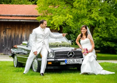 Brautpaar vor schwarzem Oldtimer bei Königsdorf, Hochzeitsshooting im Freien, Braut mit Blumenstrauß, fröhliche Szenen.