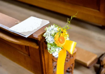 Blumendekoration mit gelbem Band an Kirchenbank bei kirchlicher Trauung in Bad Toelz, Hochzeitsfotografie.