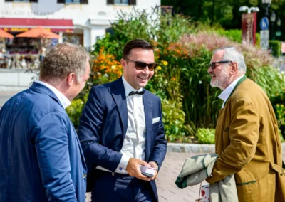 Drei Herren in Anzuegen bei einer Hochzeit vor gruenem Hintergrund am Tegernsee, entspanntes Gespraech.