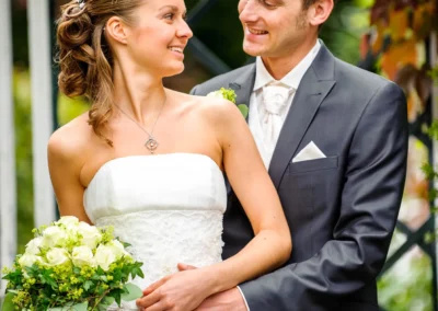 Brautpaar laechelt sich an, Braut mit Blumenstrauss. Hochzeitsfoto in Pullach bei der Hochzeit.