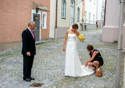 Braut erhält Hilfe beim Kleid vor kirchlicher Trauung in Bad Tölz. Hochzeitsfotograf fängt magischen Moment ein.