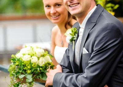 Brautpaar Fotoshooting bei einer Hochzeit in Pullach, Brautpaar laechelt und posiert mit Blumenstrauss.
