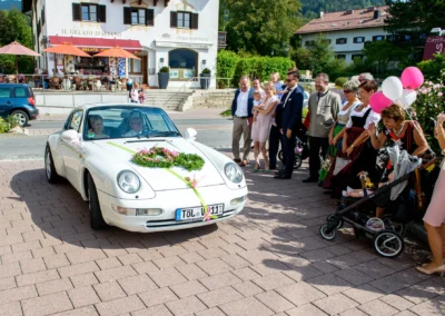 Hochzeitsauto bei Rathaus Tegernsee, umgeben von gratulierenden Gaesten. Hochzeitsfotografie in Bayern.
