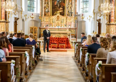Kirchliche Trauung in St. Michael, München. Gäste sitzen in dekorierter Kirche. Hochzeit in Oberbayern.