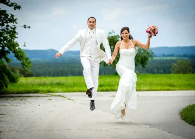 Brautpaar springt fröhlich in Hochzeitsportrait auf einer Landstraße in Königsdorf. Hochzeitsreportage südlich von München.