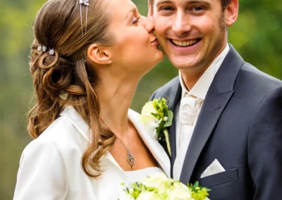 Brautpaar beim Fotoshooting, die Braut in weiss kuesst den Bräutigam. Hochzeitsfotografie in Pullach.