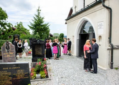 Gäste in traditioneller Kleidung vor Kirche in Wolfratshausen bei kirchlicher Trauung, Hochzeitsreportage.