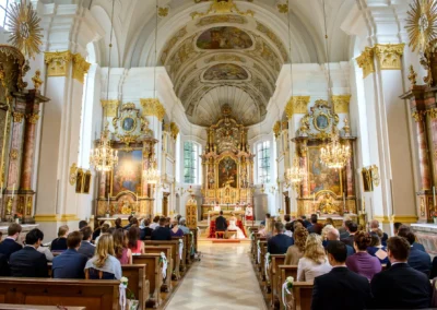 Kirchliche Trauung in St. Michael, München, Hochzeitsgaeste in Bankreihen, dekorierte Kapelle, festlicher Altar.