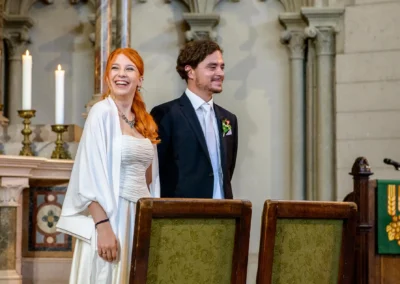 Brautpaar bei kirchlicher Trauung in Lukaskirche, lachend vor Altar. Hochzeitsfotografie in Muenchen zeigt emotionale Momente.