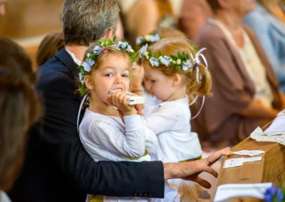 Zwei Blumenmaedchen mit Blumenkranz bei Hochzeit in Sitzreihe in Sendling, festgehalten von Hochzeitsfotografen.