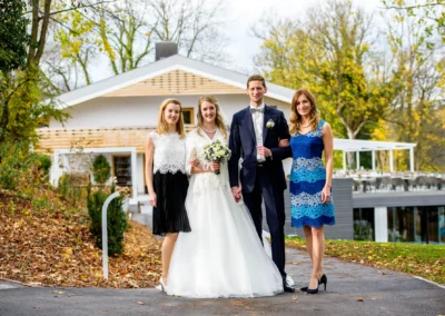 Brautpaar mit zwei Gaesten bei Hochzeitsfotografie in Bayern, Herbstlaub und modernes Haus im Hintergrund.