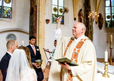 Priester segnet Brautpaar während kirchlicher Trauung in Schloss Blutenburg, Hochzeit Oberbayern. Hochzeitsreportage.