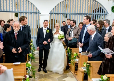 Brautpaar bei kirchlicher Trauung in St. Leonhard, Dietramszell, umgeben von Gaesten in festlicher Atmosphaere.