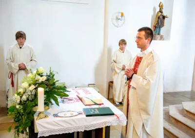 Priester und Messdiener bei kirchlicher Trauung in Solln, Hochzeitsfotografie am Altar mit Blumen und Kerze.