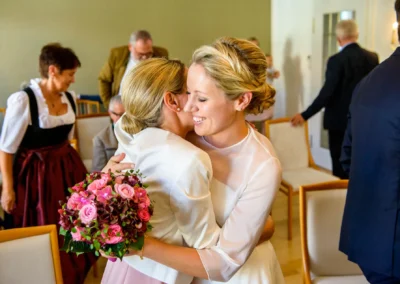 Braut umarmt jemanden mit Blumenstrauss in der Hand, Hochzeit im Rathaus Tegernsee, Hochzeitsfotografie Bayern.