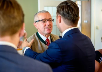 Zwei elegante Herren begrüßen sich herzlich bei einer Hochzeitsfeier im Rathaus Tegernsee.