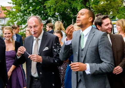 Gäste bei der Hochzeit am Pfanzeltplatz in München machen Seifenblasen vor der Kirche St. Michael. Hochzeitsreportage.