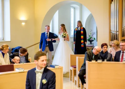 Braut betritt mit Brautvater Kirche in Bernried, waehrend Gaeste der Trauung zusehen. Hochzeitsfotografie in Bayern.