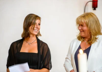 Zwei Frauen lachen bei der kirchlichen Trauung in Obermenzing, festgehalten in einer Hochzeitsreportage.